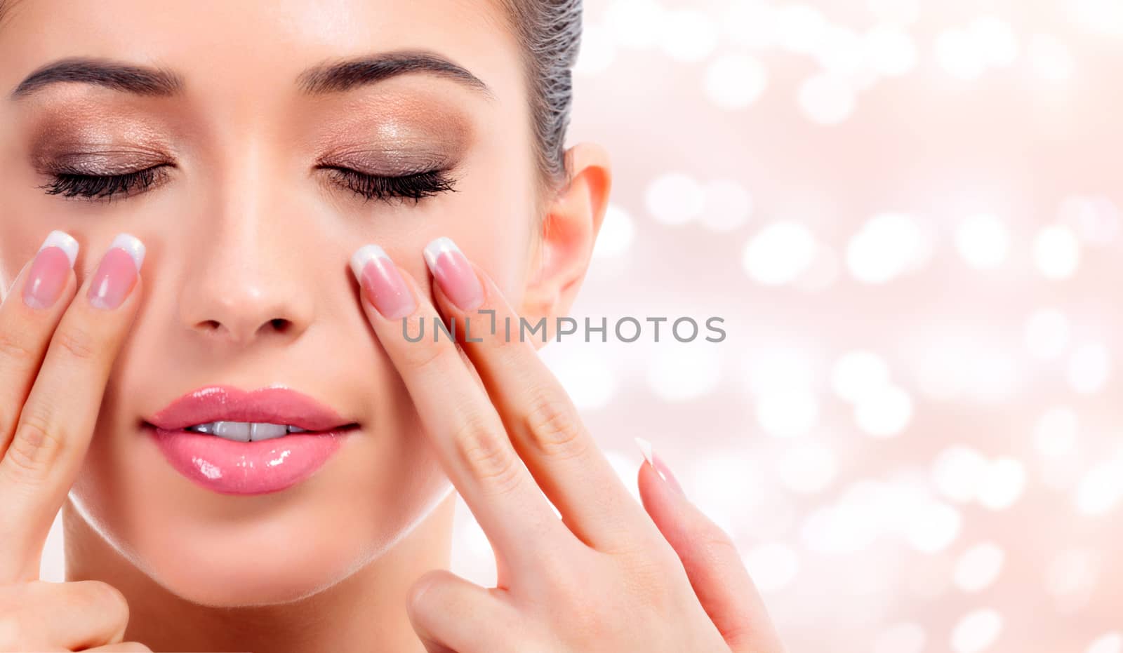 Pretty woman massaging her face, skin treatment concept. Abstract background with blurred lights