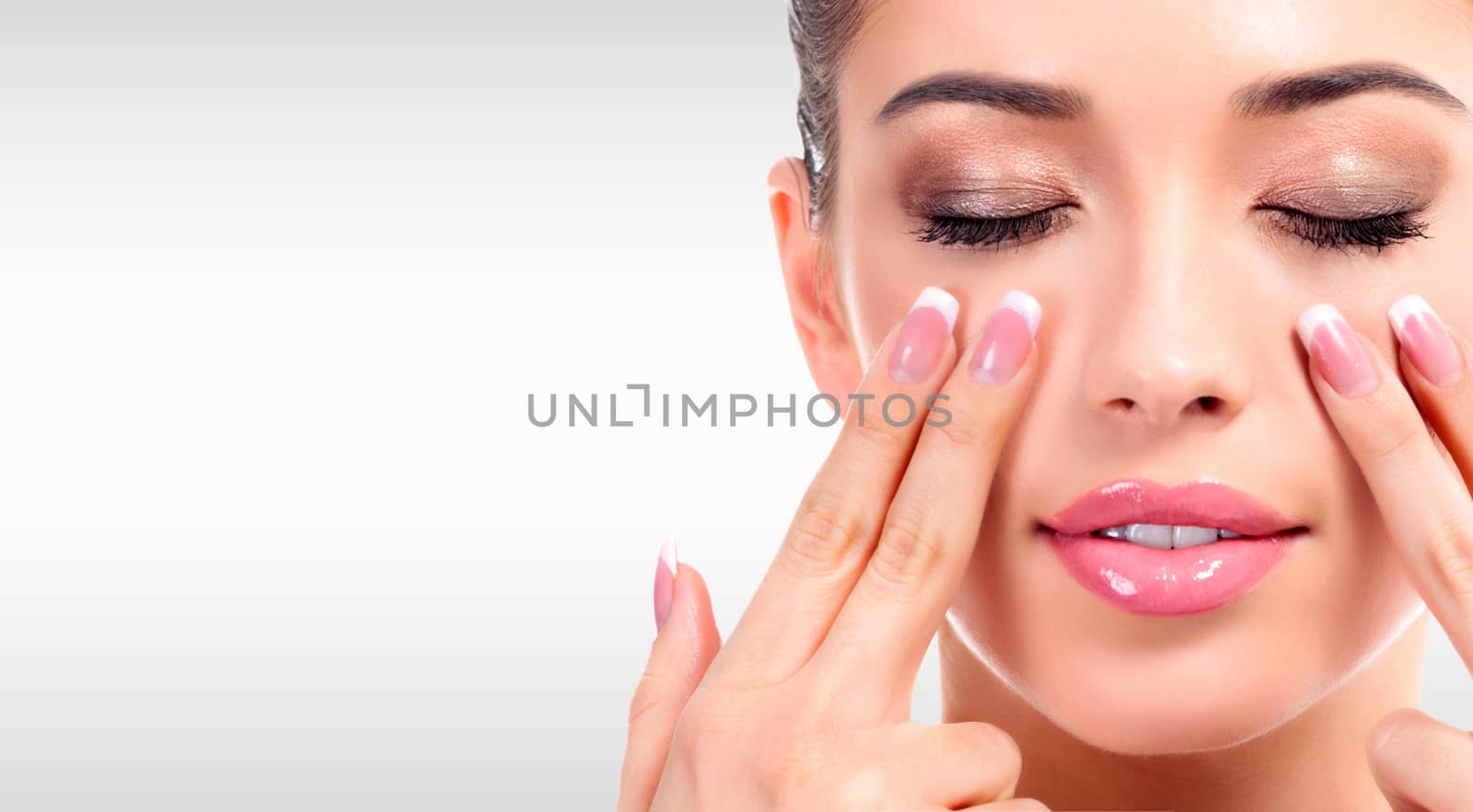 Closeup shot of young beauty woman massaging her face. Facial massage concept. Pretty girl against a grey background with copyspace