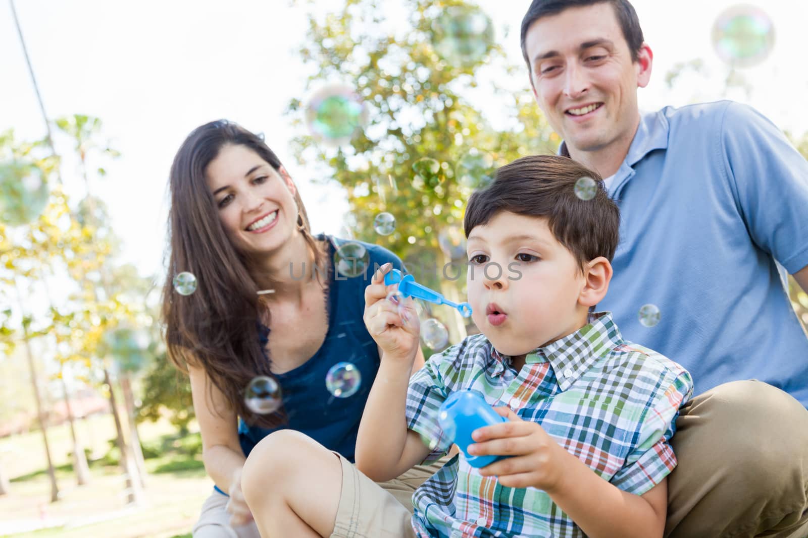 Young Boy Blowing Bubbles with His Parents in the Park.