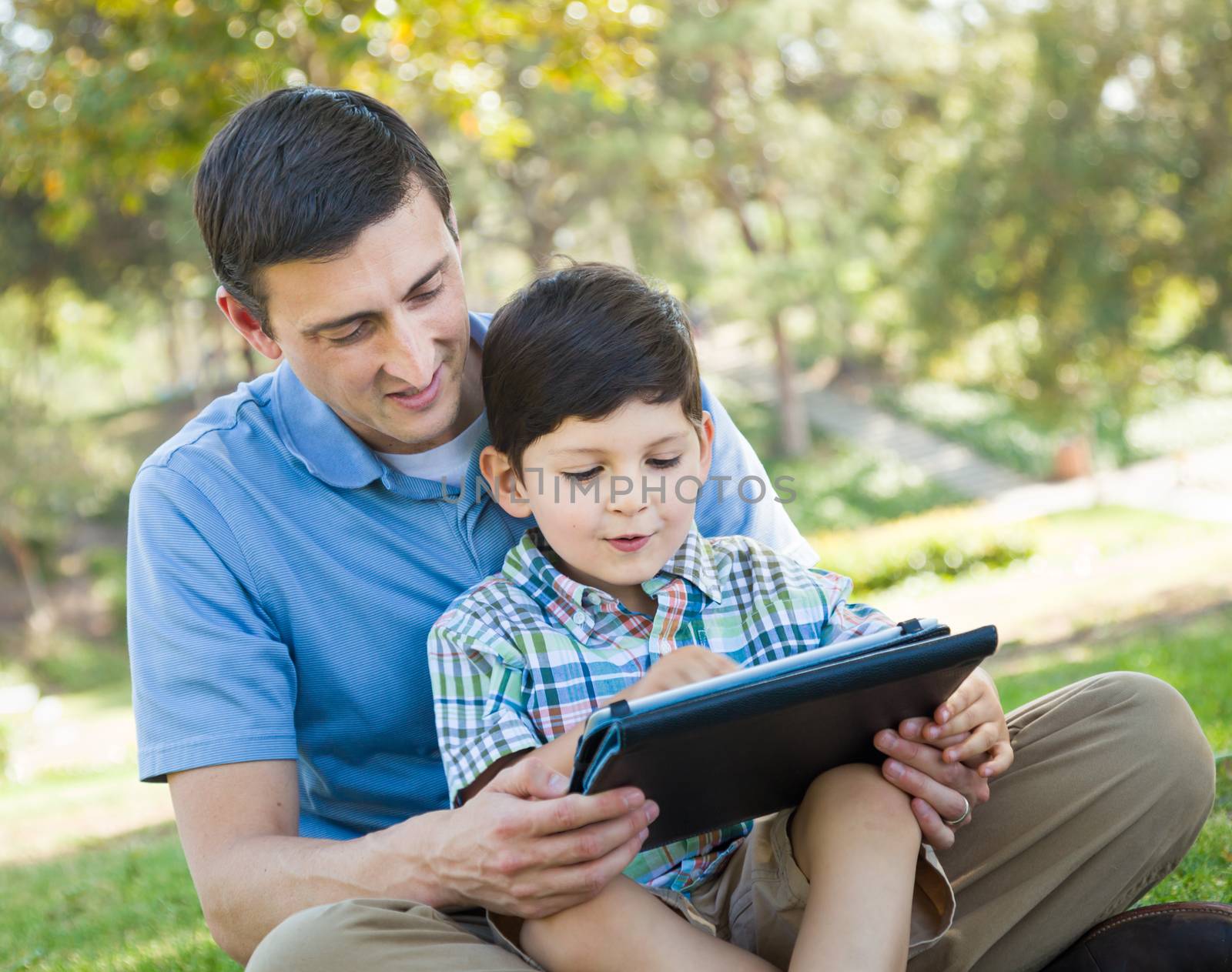 Happy Father and Son Playing on a Computer Tablet Outside.