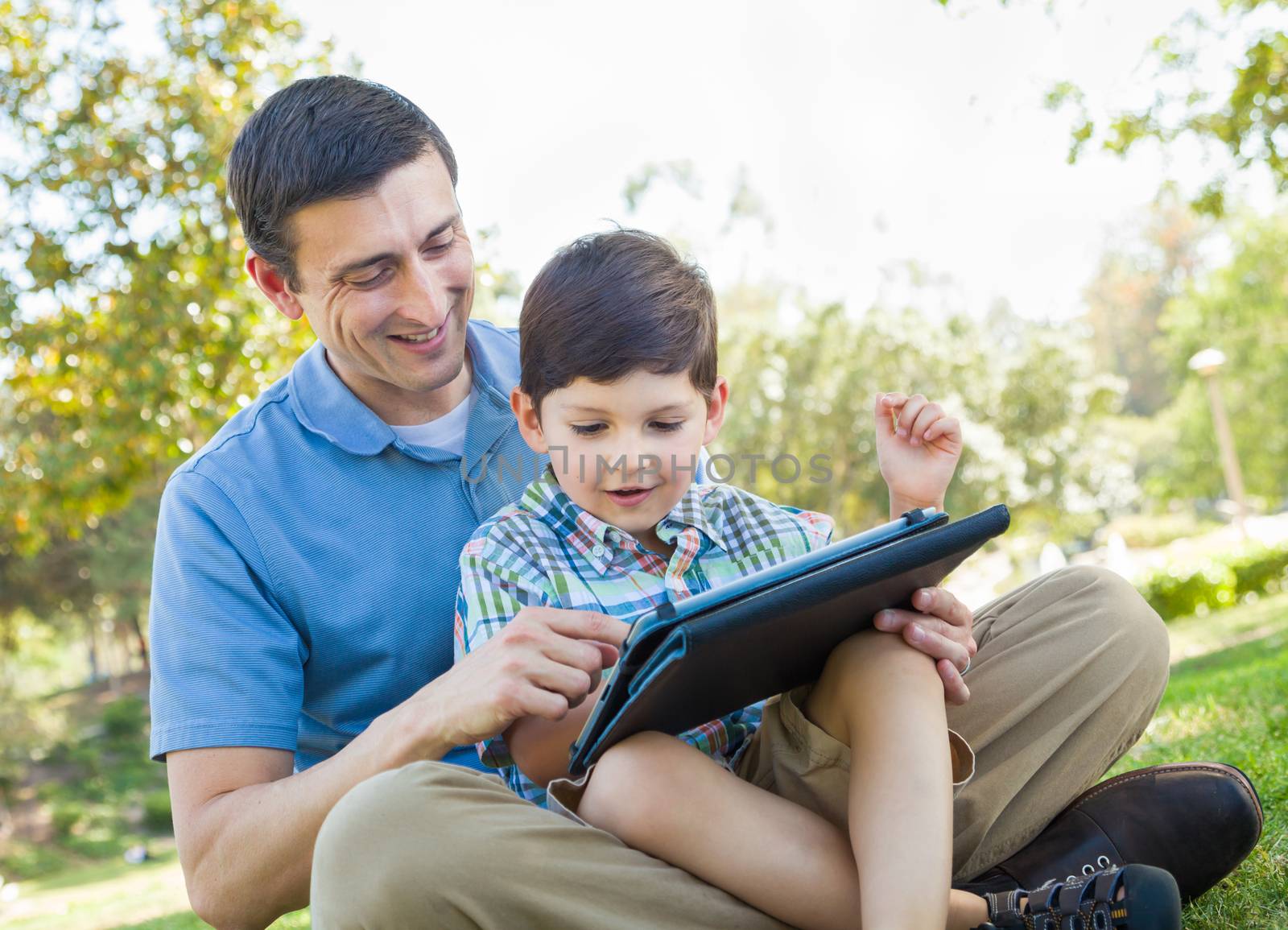 Happy Father and Son Playing on a Computer Tablet Outside.