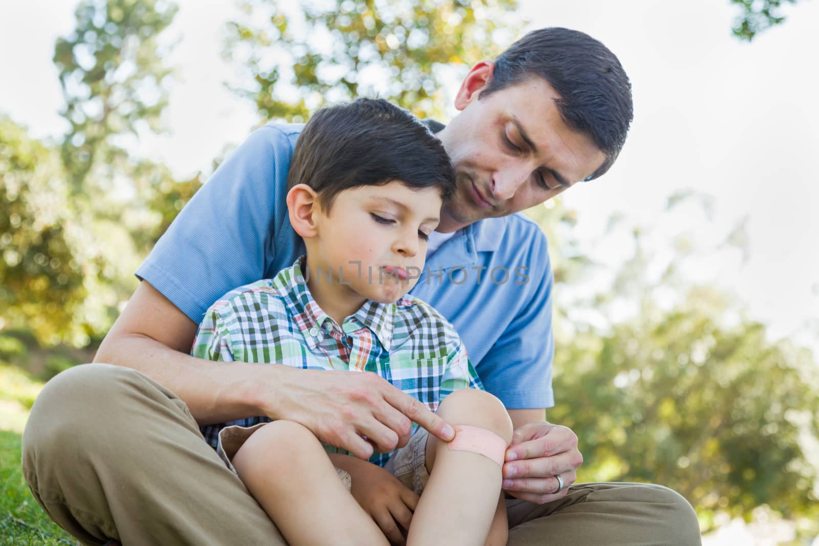 Loving Father Puts a Bandage on the Elbow of His Young Son in the Park.