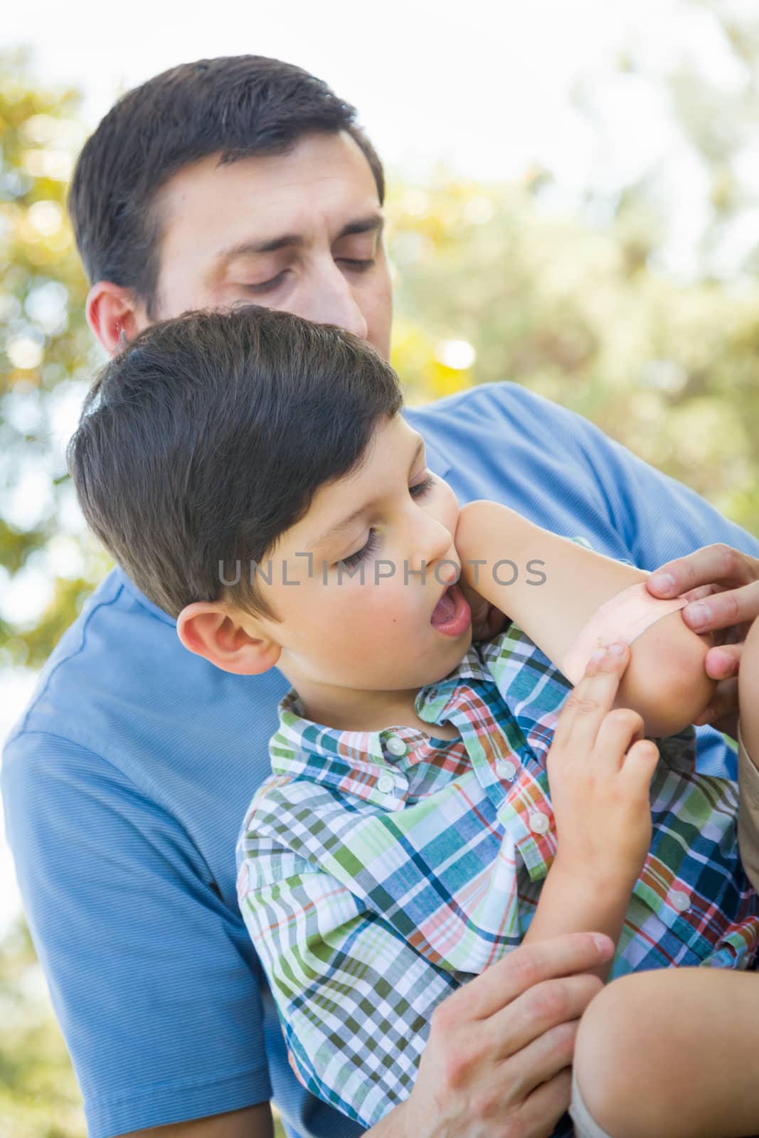 Loving Father Puts a Bandage on the Elbow of His Young Son in the Park. by Feverpitched