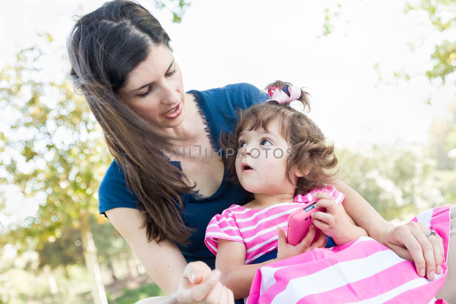 Mixed Race Mother and Cute Baby Daughter Playing with Cell Phone in Park.