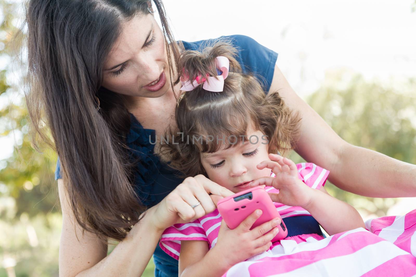 Mixed Race Mother and Cute Baby Daughter Playing with Cell Phone in Park.