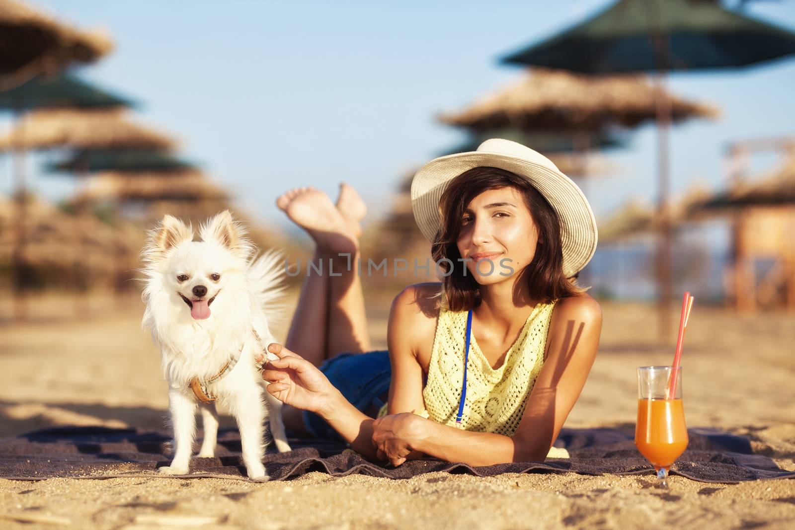 beautiful girl enjoying cocktail on a beach with her puppy