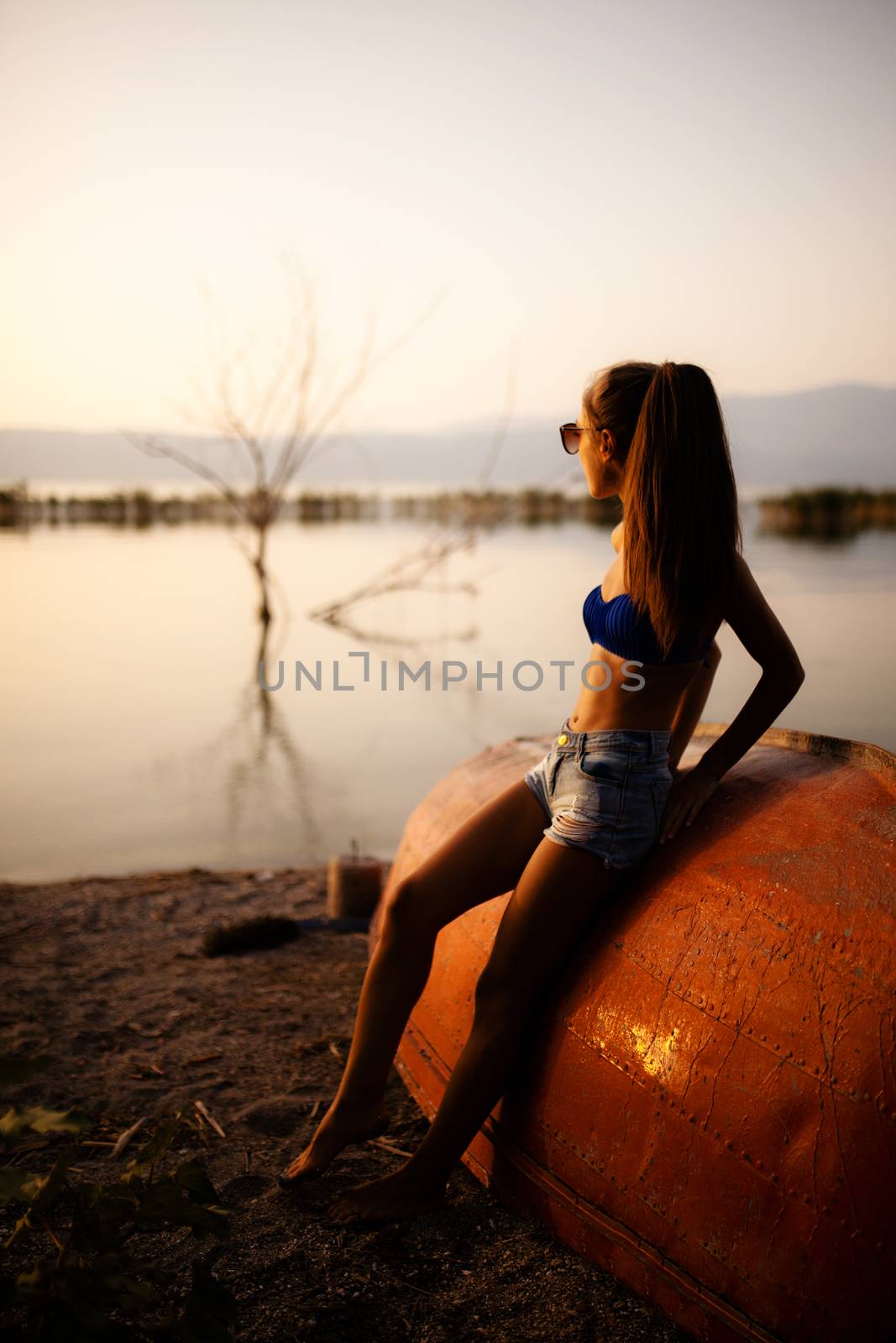 beautiful girl on a rowboat looking at sunset on a lake. half silhouette shot
