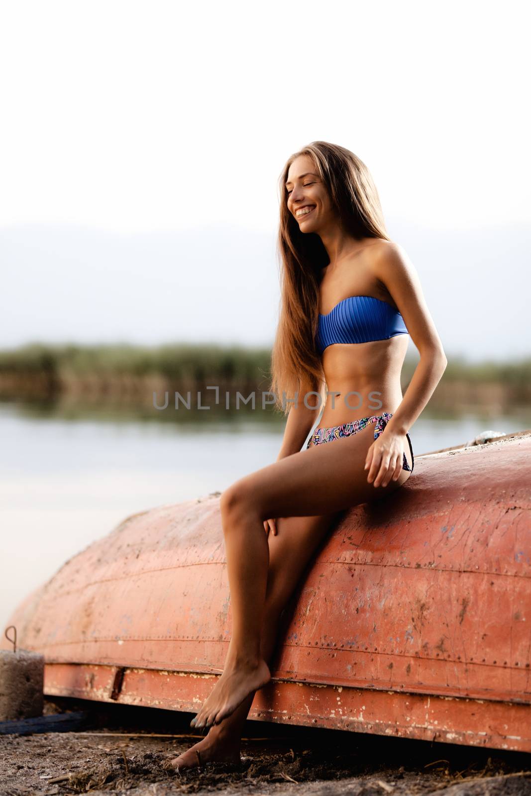 beautiful girl on an upturned rowboat smiling and enjoying a sunset