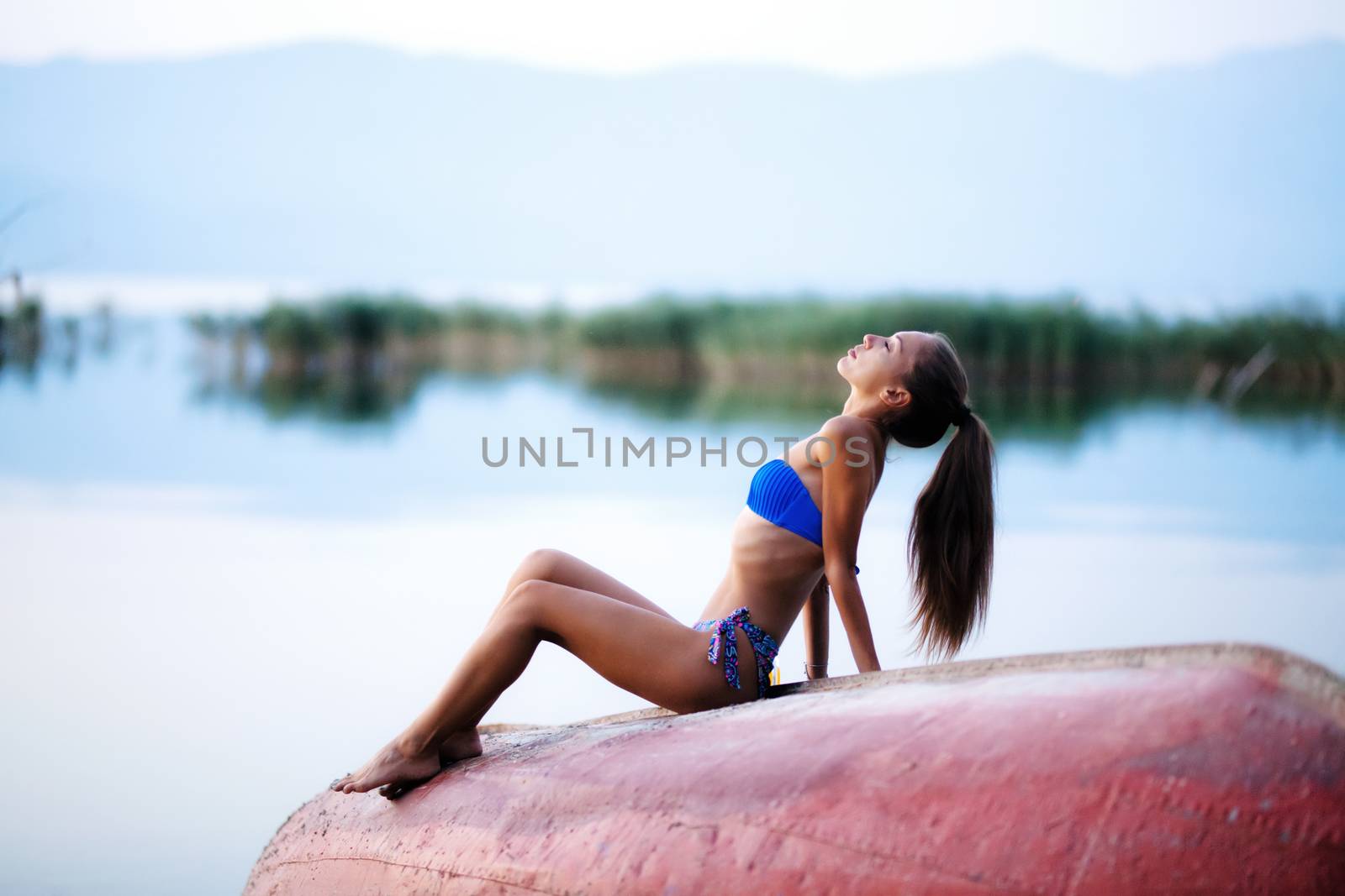 beautiful girl on a rowboat, sunset time on a lake. full body shot