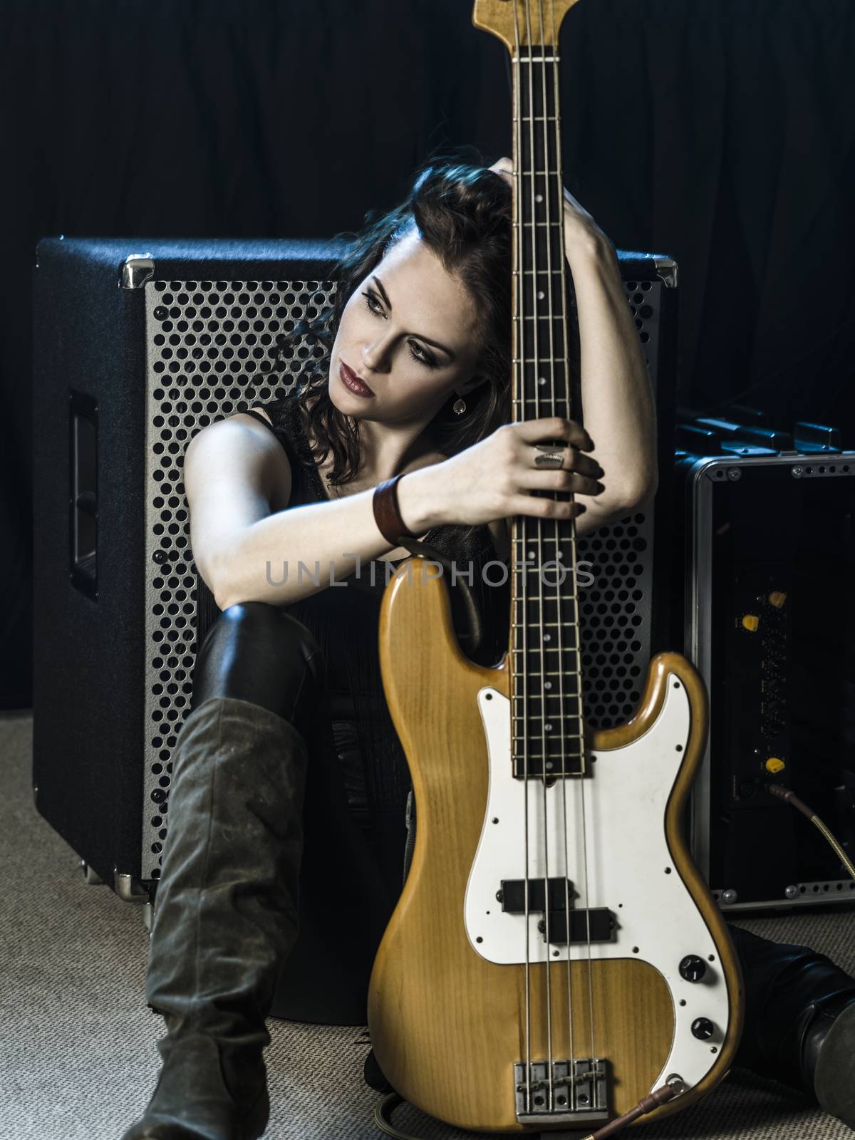 Photo of a beautiful woman bass player sitting in front of her amplifier.