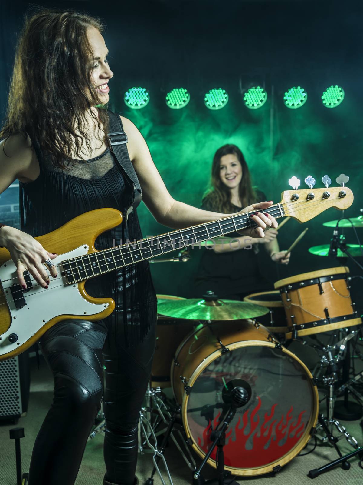 Photo of a female bass player and drummer of a rock band playing on stage.