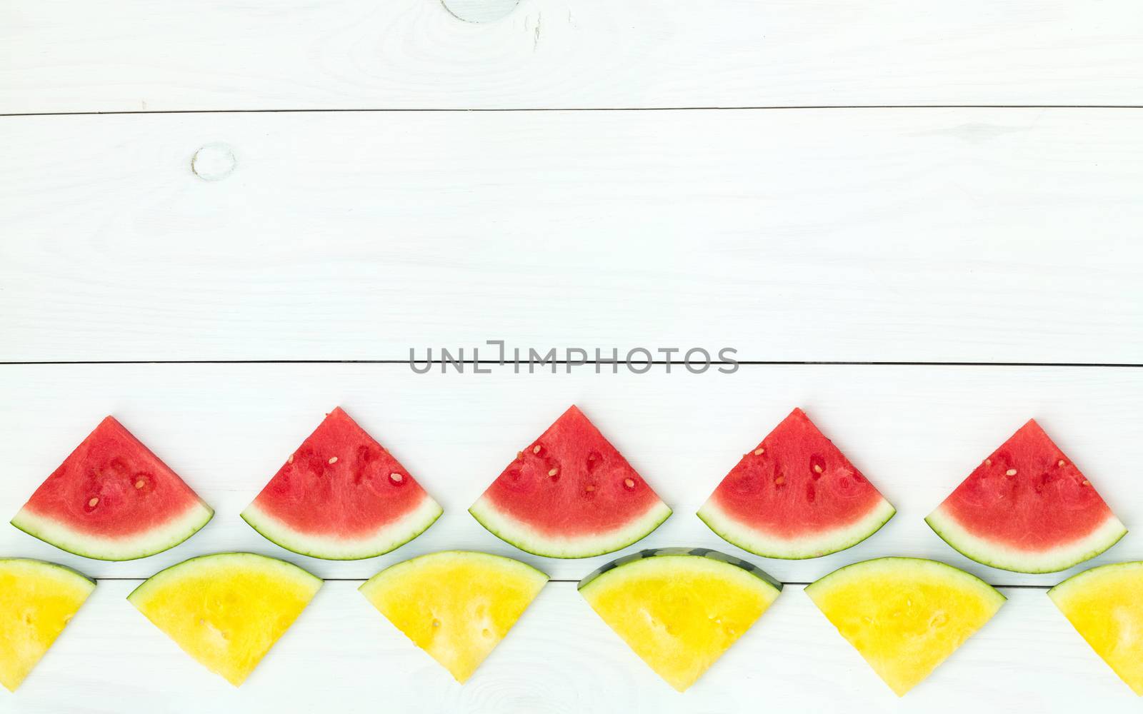 Red and yellow watermelon slices on wooden sticks on a white wooden background. Flat lay, top view, copy space