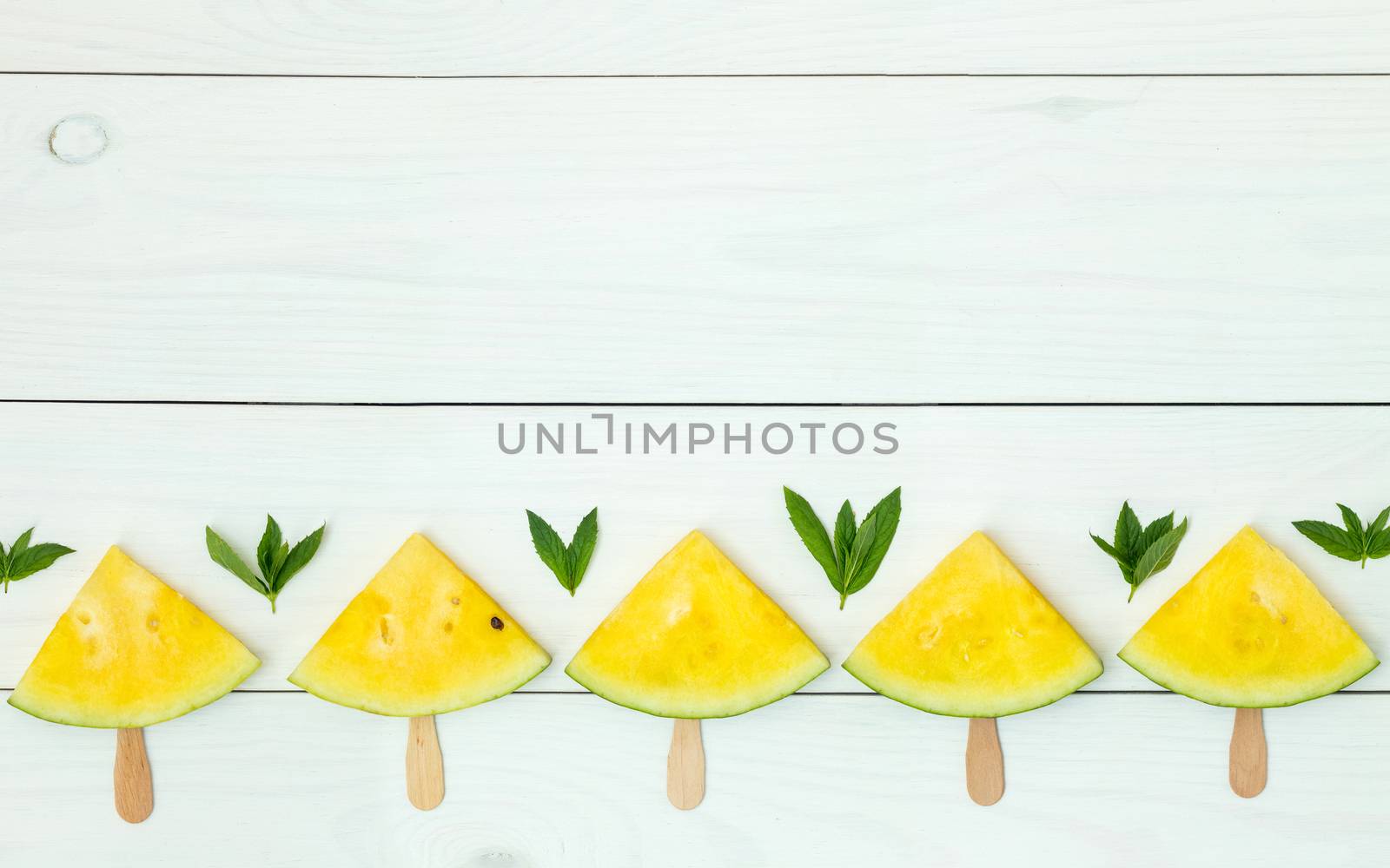 Bright yellow watermelon slices on wooden sticks on a white wooden background. Flat lay, top view, copy space