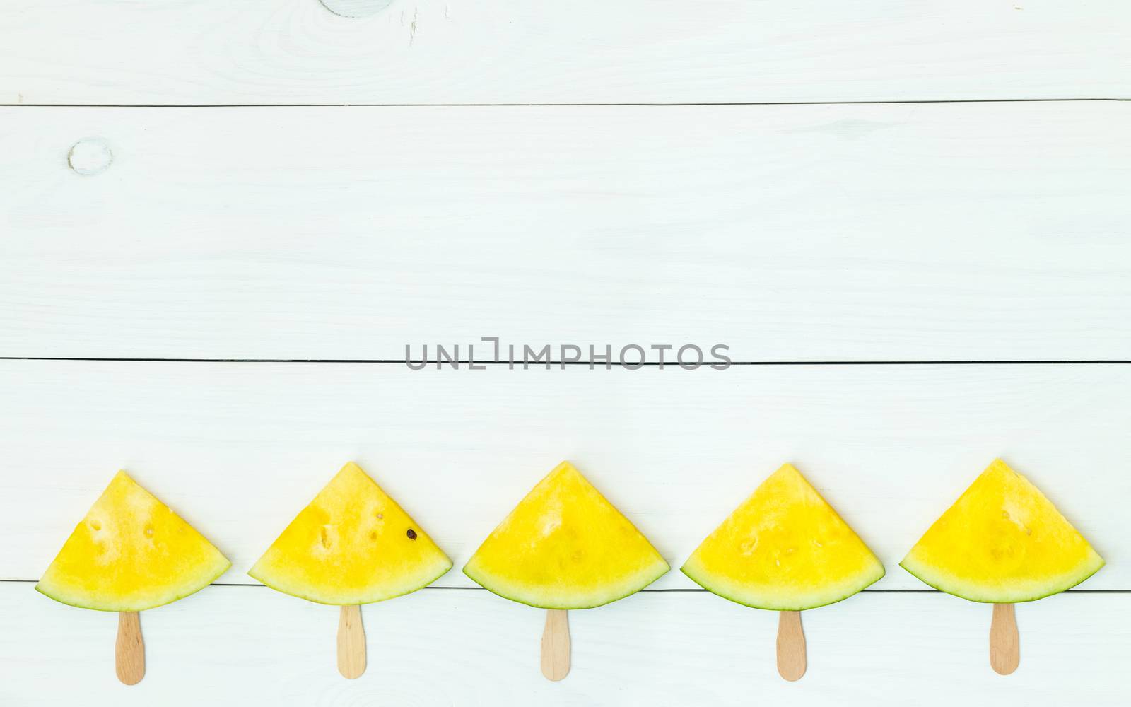 Bright yellow watermelon slices on wooden sticks on a white wooden background. Flat lay, top view, copy space