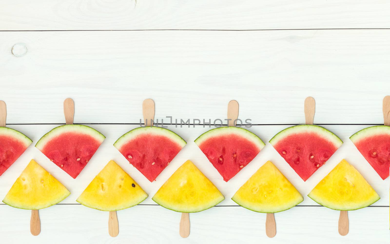 Red and yellow watermelon slices on wooden sticks on a white wooden background. Flat lay, top view, copy space