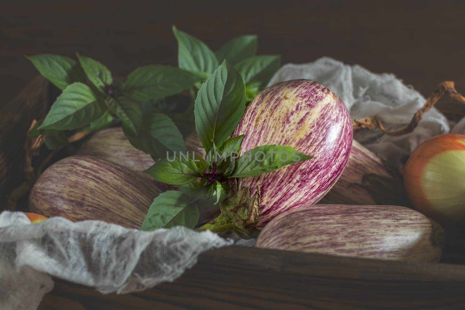 Purple graffiti eggplants, onion and green fresh basil in a wooden box in a vintage wooden background in rustic style, selective focus