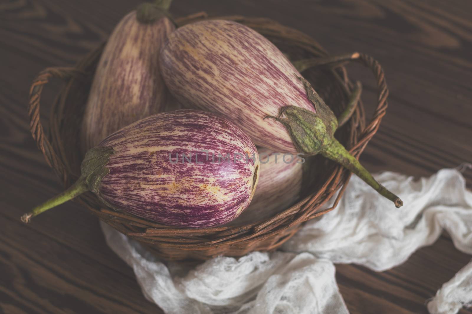 Purple graffiti eggplants in a wicker basket in a vintage wooden background in rustic style, selective focus