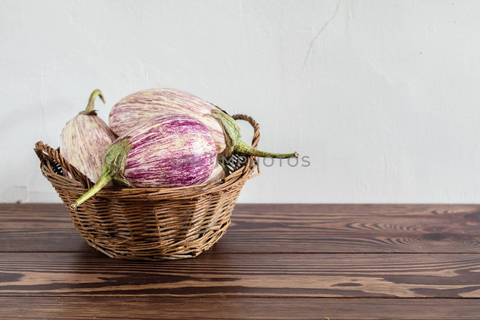 Purple graffiti eggplants in a wicker basket in a vintage wooden background in rustic style, selective focus