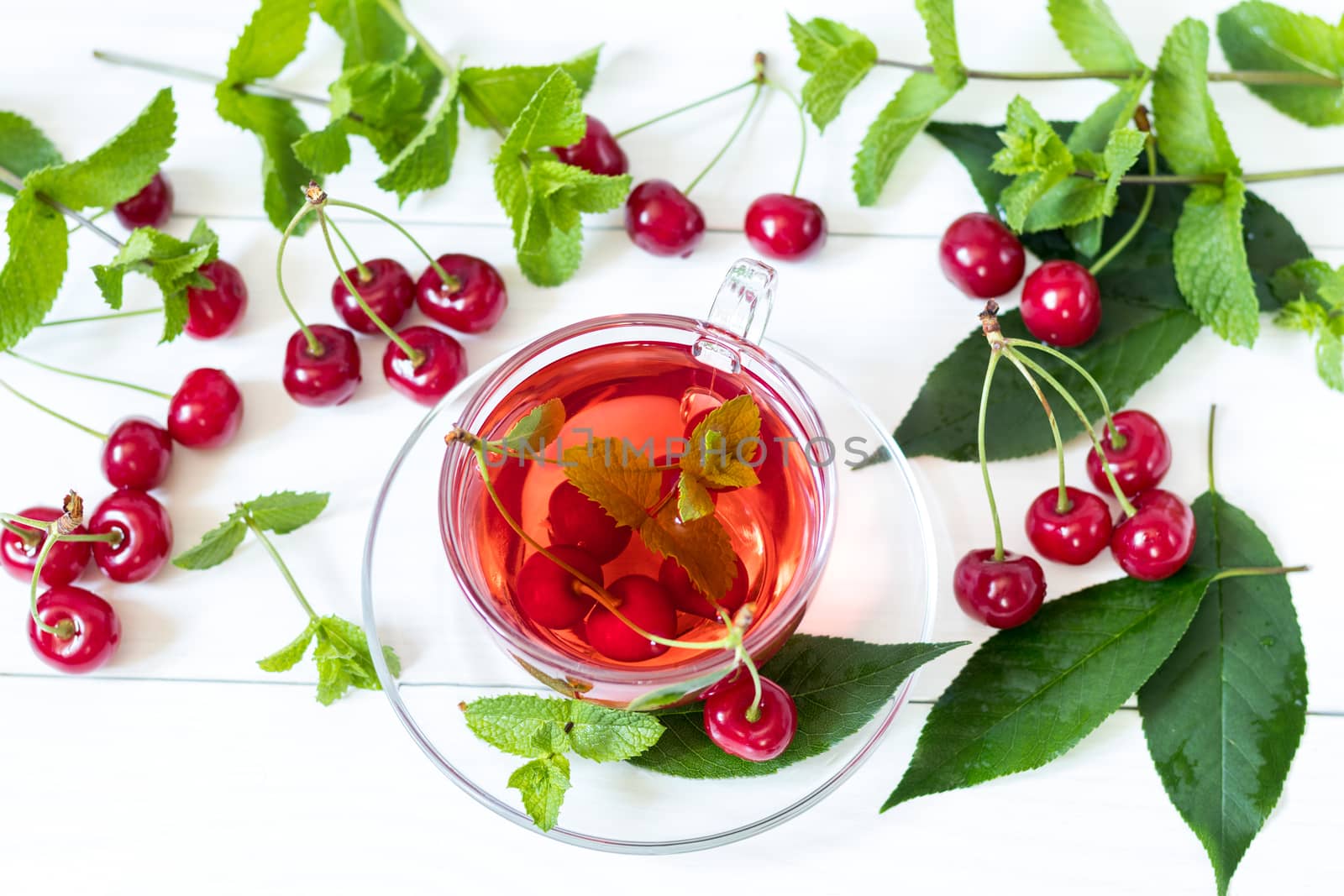 Fresh fruit cherry drink in transparent glass cup surrounded by cherries on the white wooden background. Top view