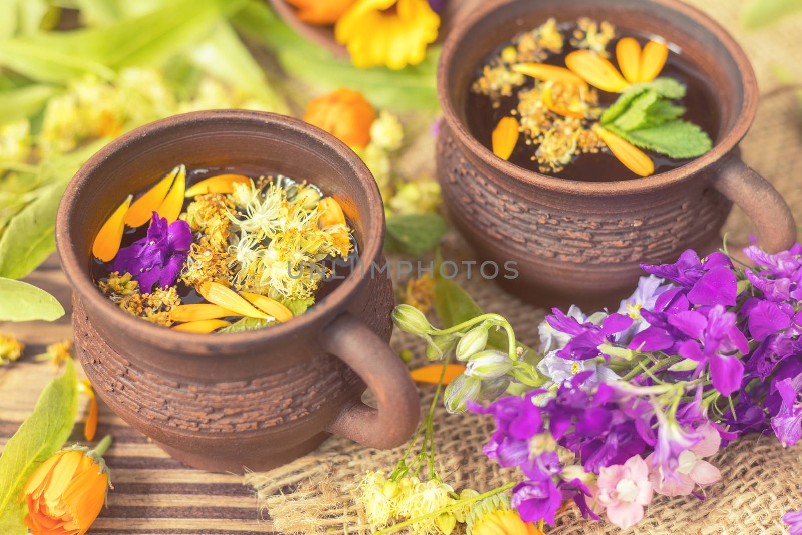 Two ceramic cups of healthy herbal tea with decoction of dry and fresh flowers on dark aged rustic wooden background. Shallow depth of field.