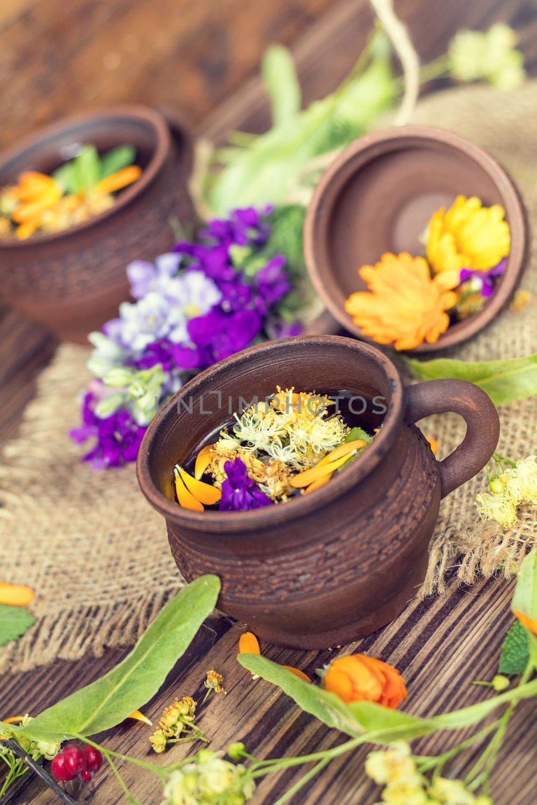 Two ceramic cups of healthy herbal tea with decoction of dry and fresh flowers on dark aged rustic wooden background. Shallow depth of field.
