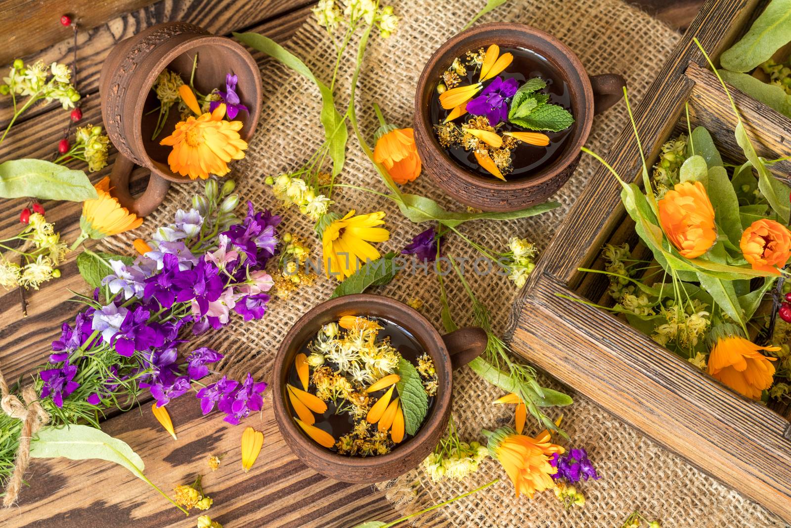 Two ceramic cups of healthy herbal tea with decoction of dry and fresh flowers on dark aged rustic wooden background. Shallow depth of field.