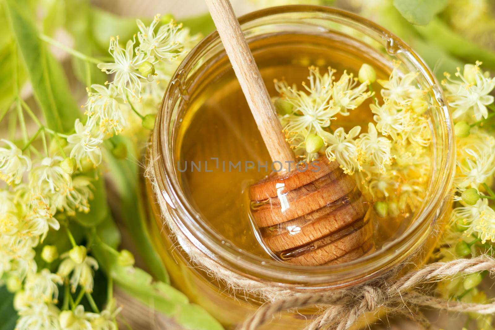 Honey in glass jars with white linden flowers on light wooden background. Shallow depth of field.