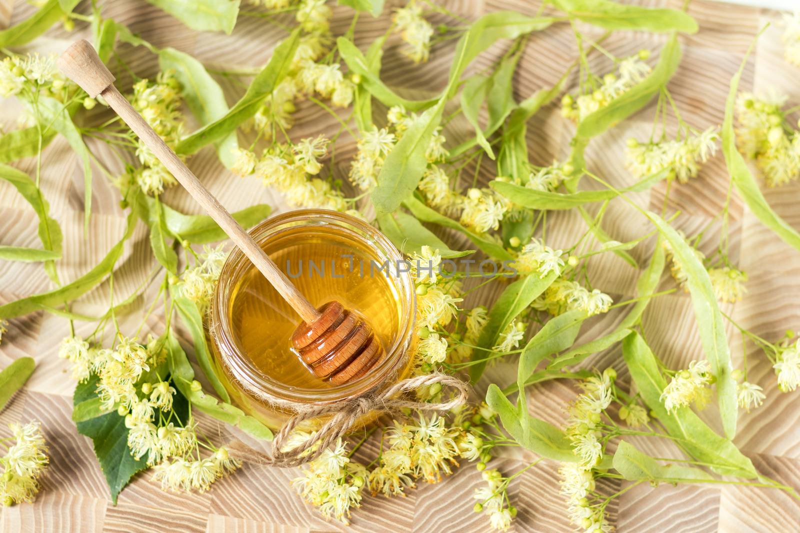 Honey in glass jars with white linden flowers on light wooden background. Shallow depth of field.