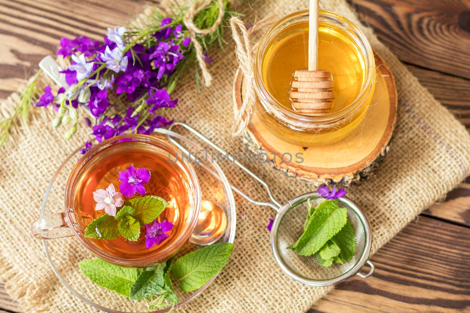 Glass cup of summer herbal tea with fresh mint and field larkspur. Jar of honey. Wooden table. Shallow depth of field.