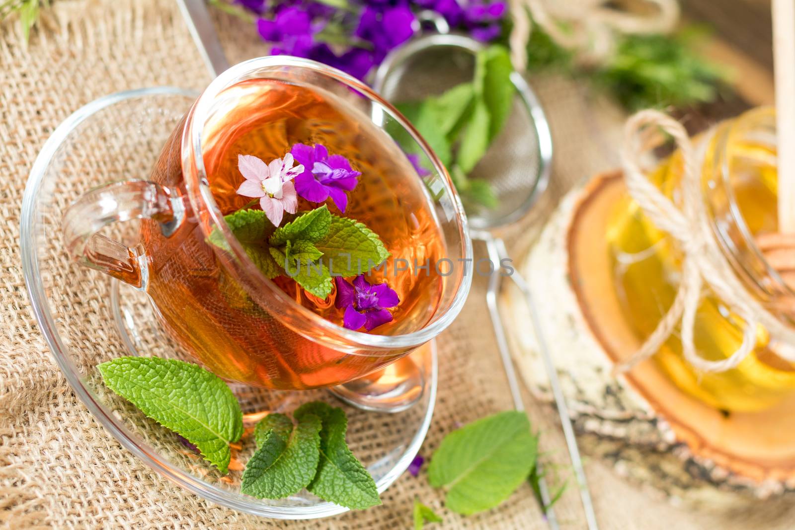 Glass cup of summer herbal tea with fresh mint and field larkspur. Jar of honey. Wooden table. Shallow depth of field.