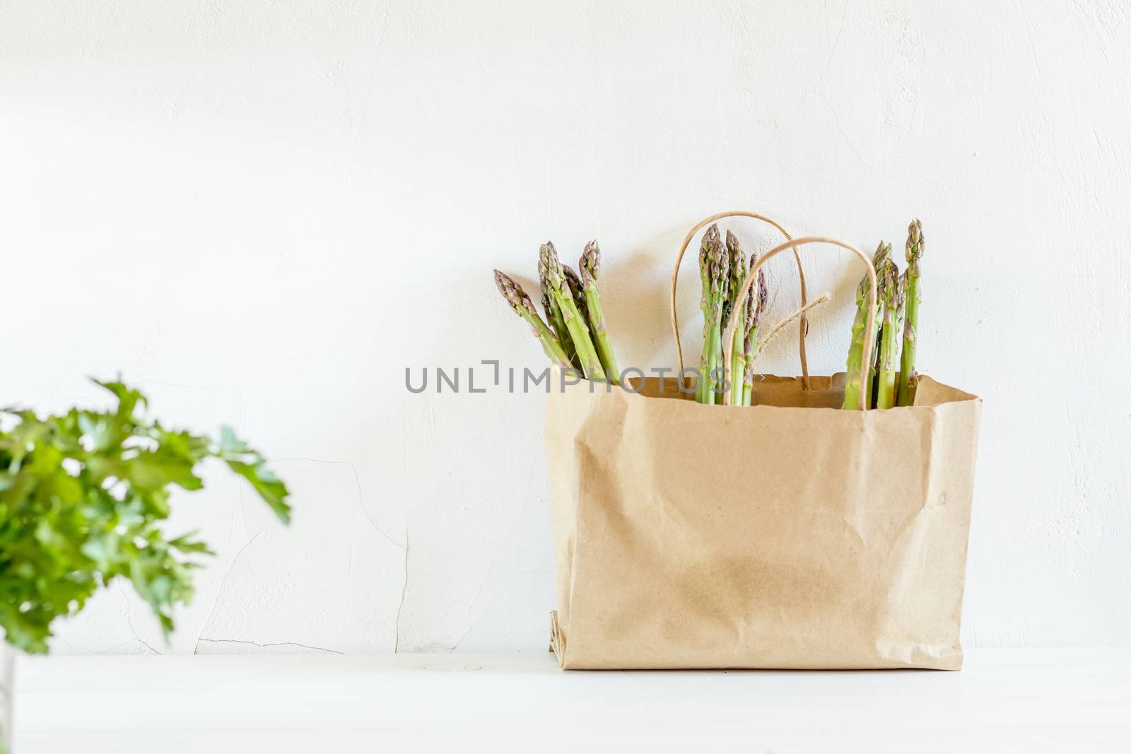 Bunches of fresh asparagus in a paper bag on white cracked wallbackground. Copy space