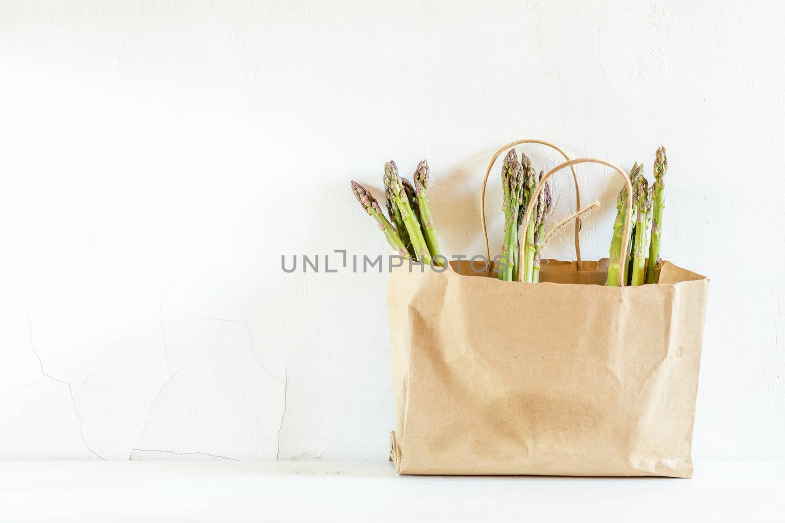 Bunches of fresh asparagus in a paper bag on white cracked wall background. Copy space