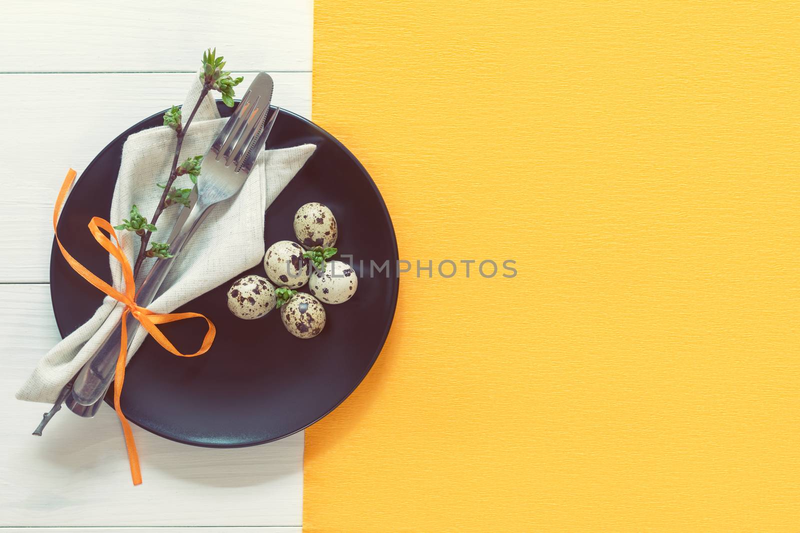 Easter table setting with spring flowers and cutlery. Rustic orange table cloth on white wood background. Holidays background with copy space.
