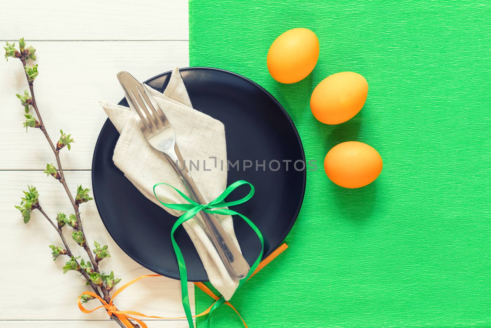 Easter table setting with spring flowers and cutlery. Rustic green table cloth on white wood background. Holidays background with copy space.