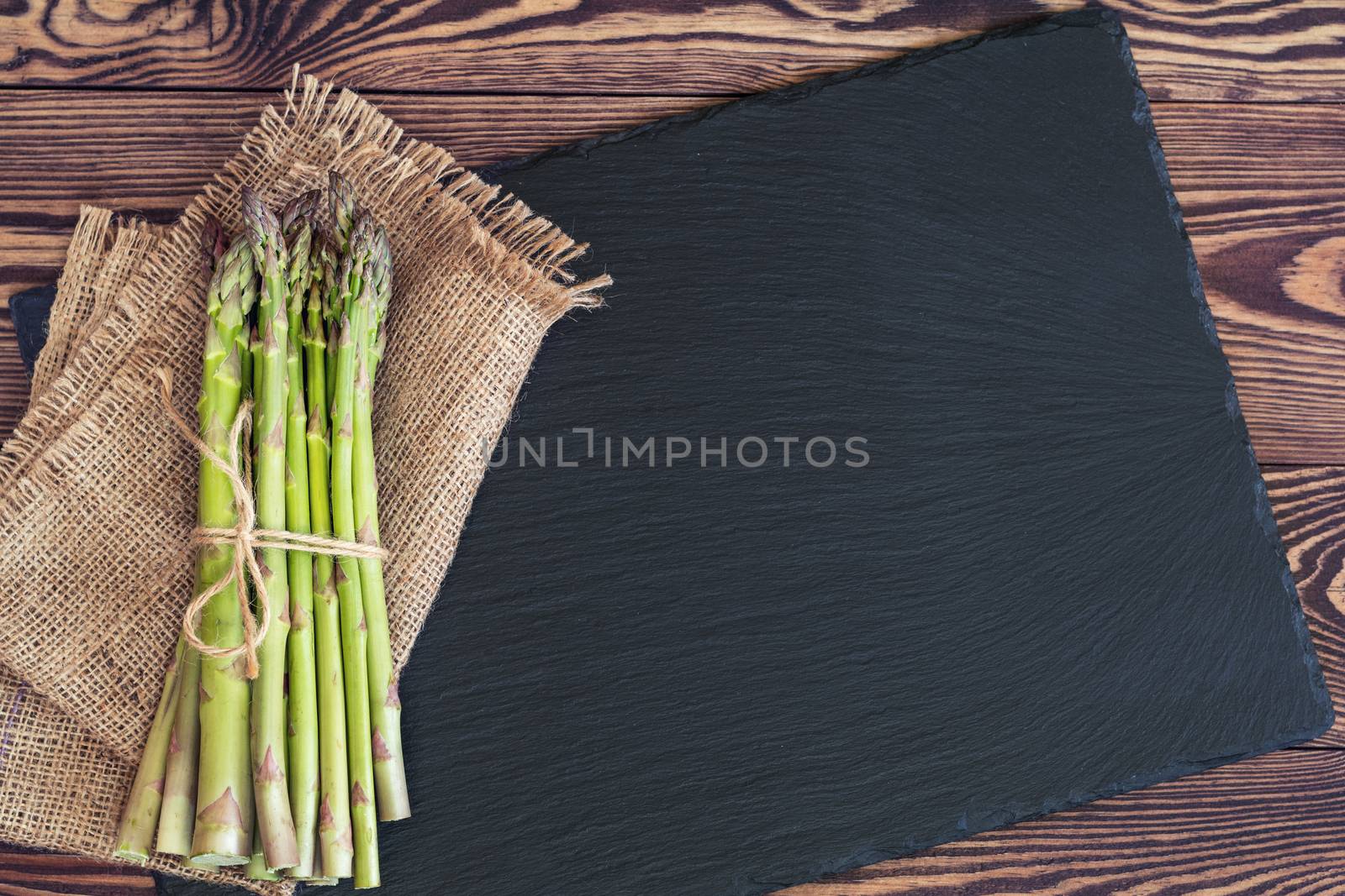 Bunch of fresh green asparagus spears on black stone on a rustic wooden table