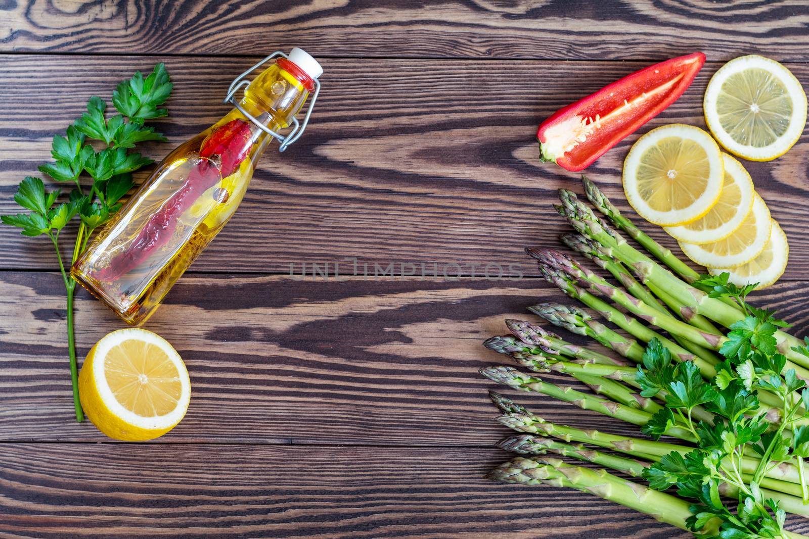 Bottle of olive oil with spices, bunch of fresh green asparagus spears and lemon on a rustic wooden table