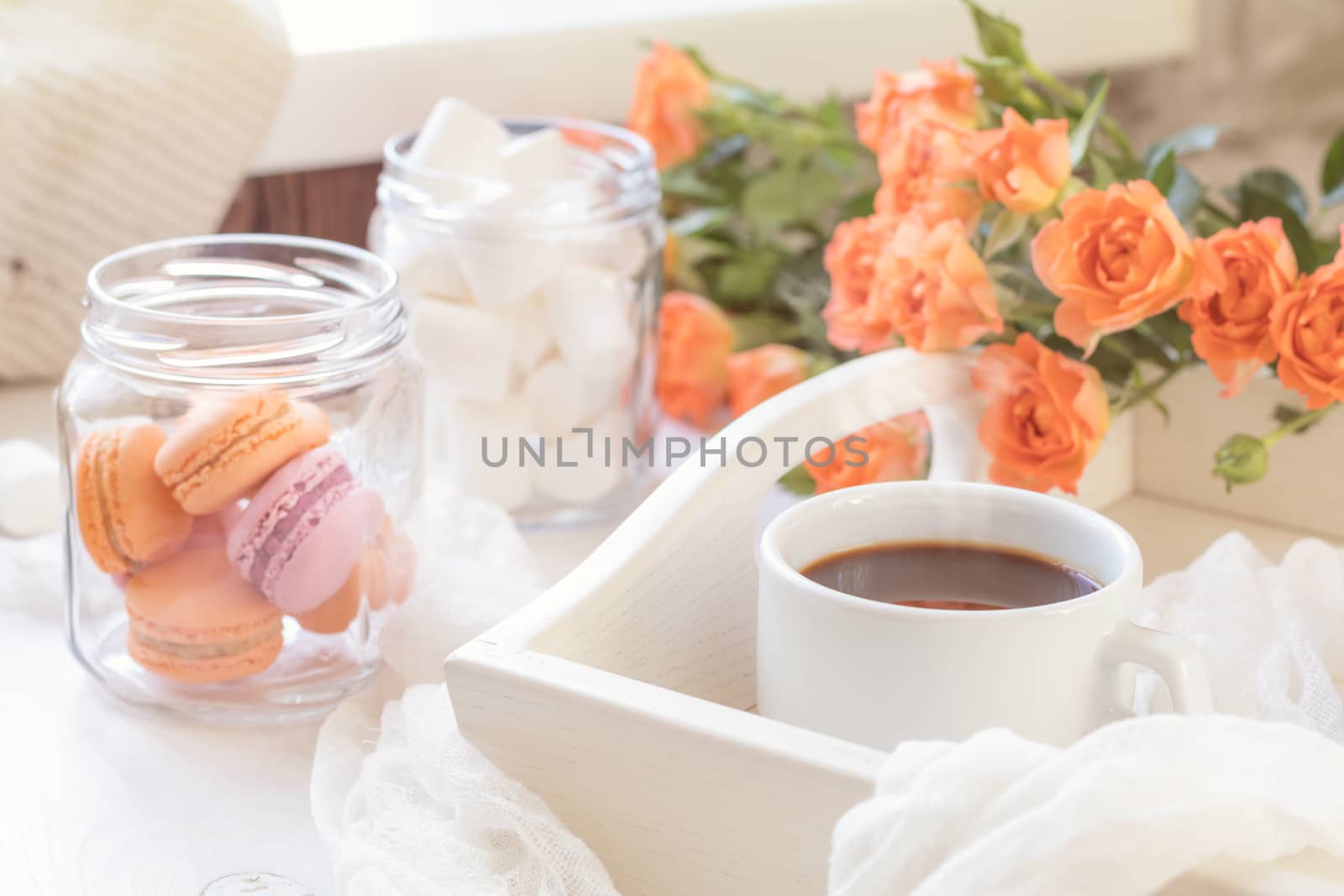 Orange mango macaroons, cup of coffee, marshmallow and fresh little roses on light wooden background. Sunlight. Coloring and processing photo with light vintage style. Shallow depth of field.