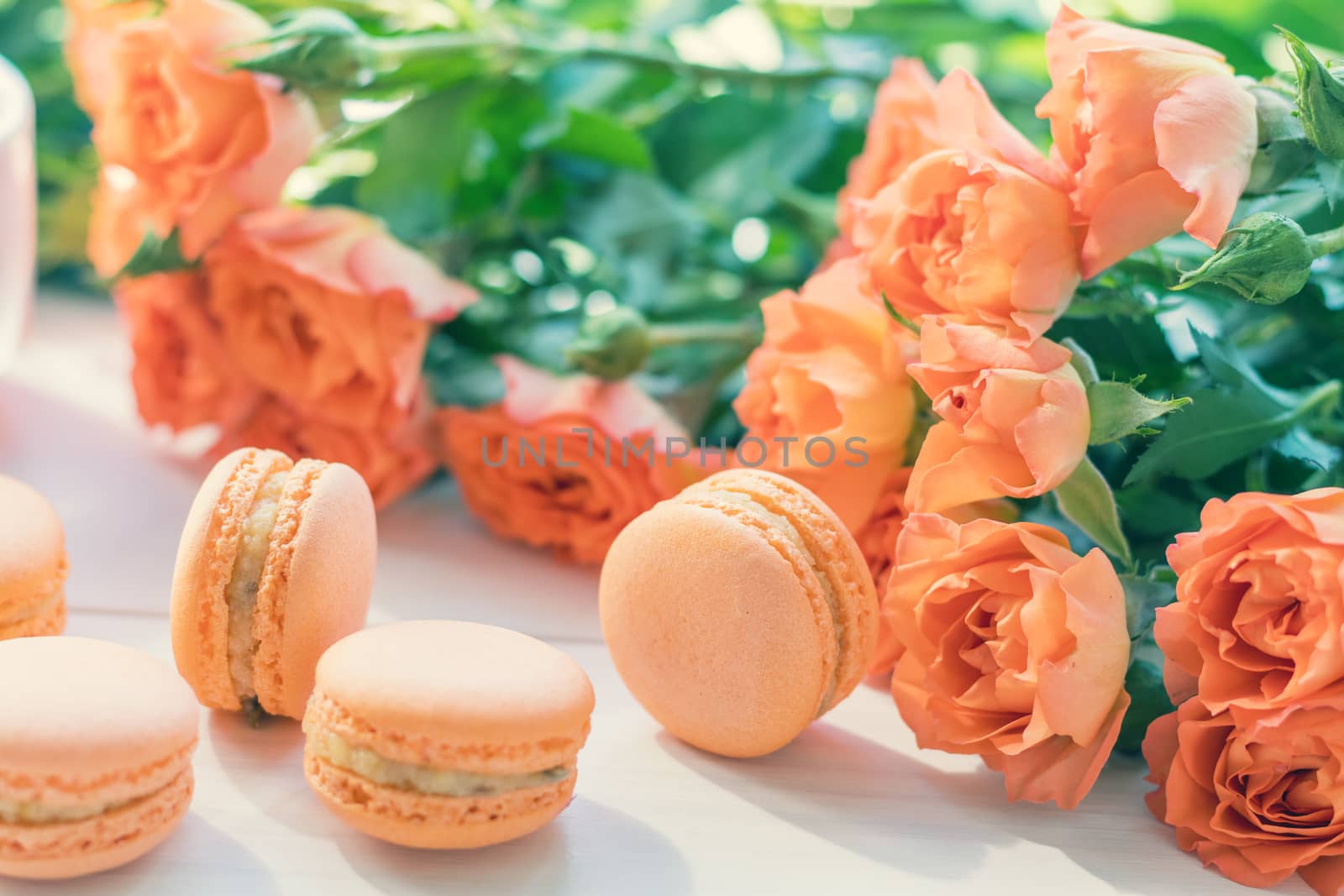 Orange mango or citrous macaroons and orange fresh little roses on light wooden background. Coloring and processing photo with light vintage style. Toned. Shallow depth of field.