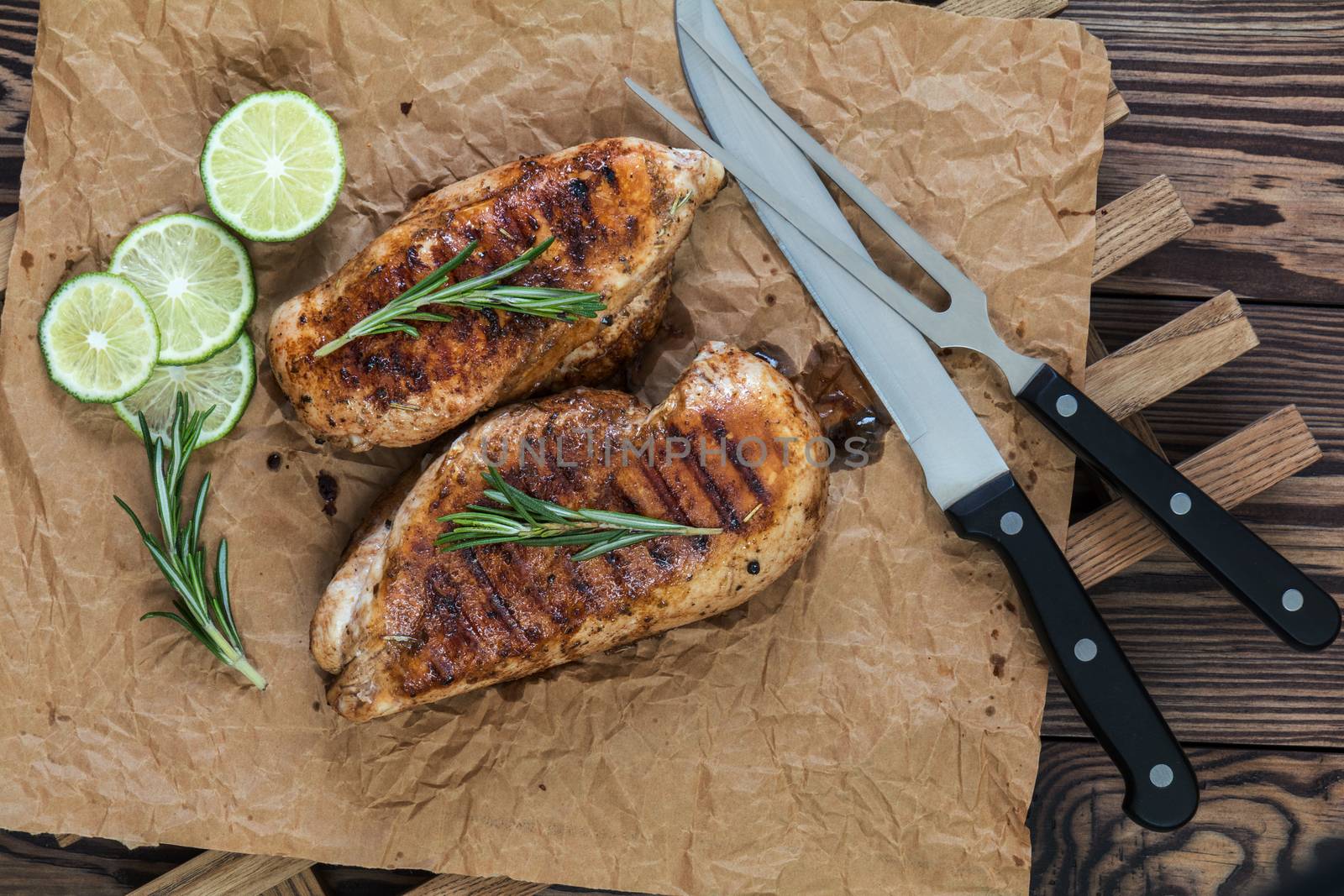 Grilled chicken filet with herbs  on a paper on wooden background. Rosemary and sliced lime on a dark groundwork.