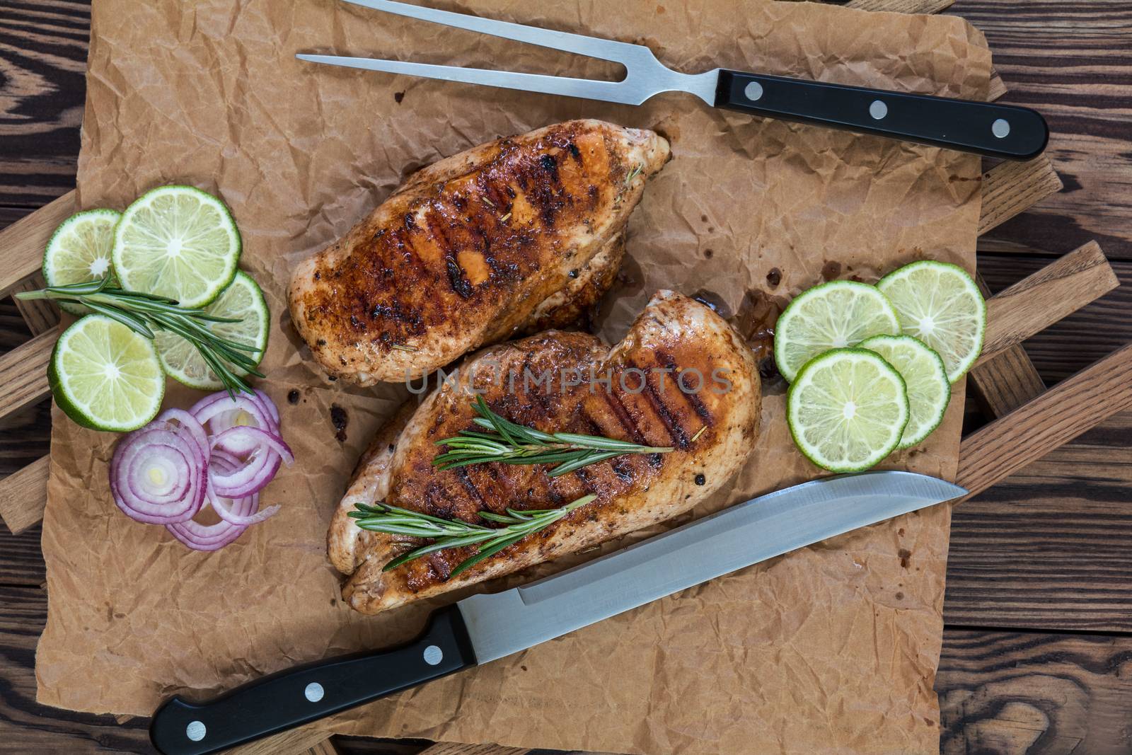 Grilled chicken filet with herbs  on a paper on wooden background. Rosemary and sliced lime on a dark groundwork.