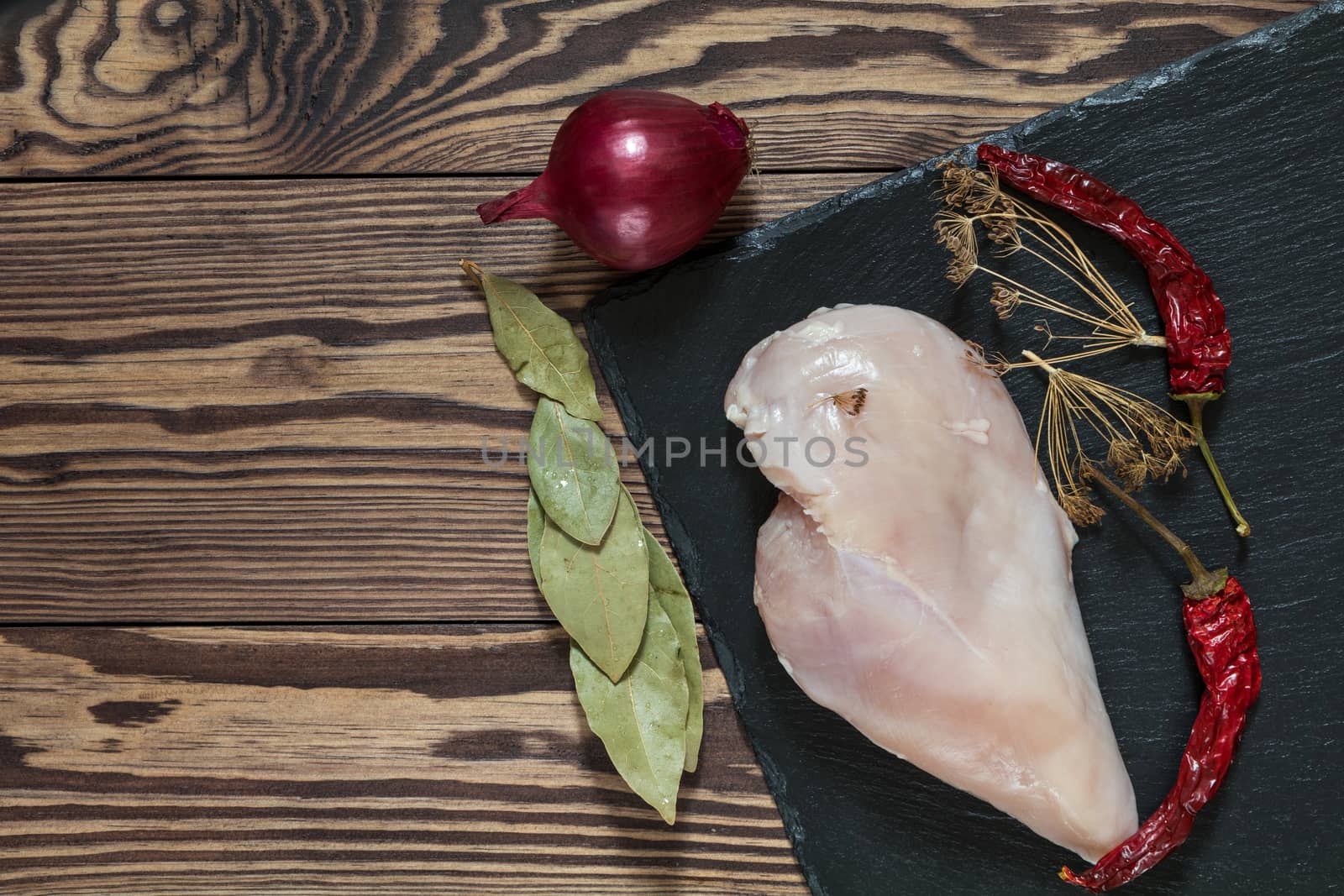 Raw uncooked chicken fillet on a cutting table with ingredients for cooking, on black stone board. Top view. Toned. Copy space.