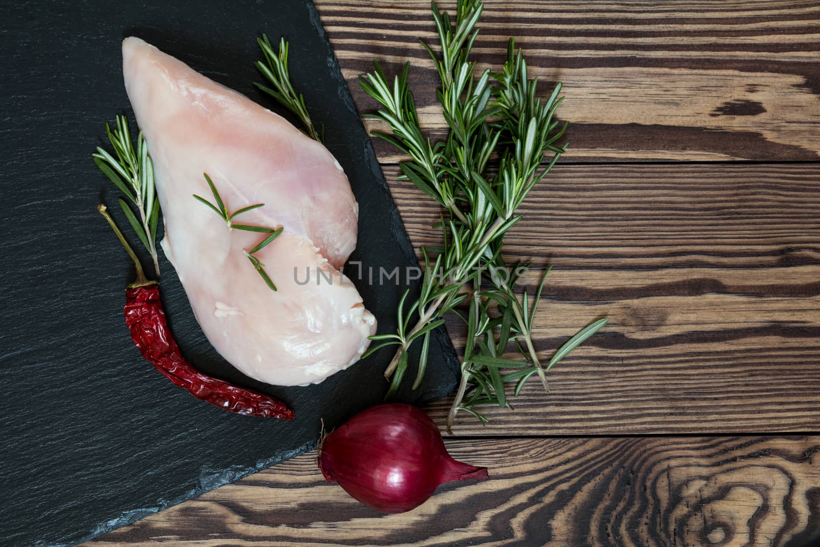 Raw uncooked chicken fillet on a cutting table with ingredients for cooking, on black stone board. Top view. Toned. Copy space.