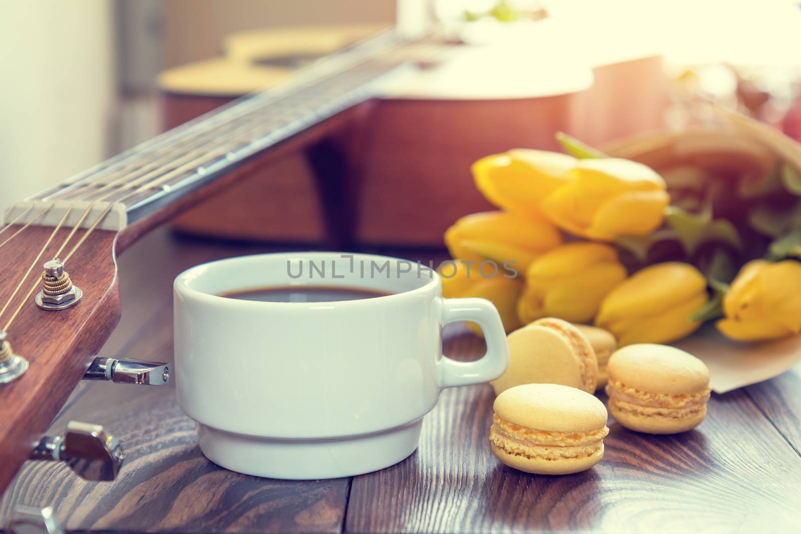 Beautiful spring music background. Cup of coffww, guitar, yellow tulips, musical page on a dark wooden background. Shallow depth of field. Coloring photo with soft focus in instagram style