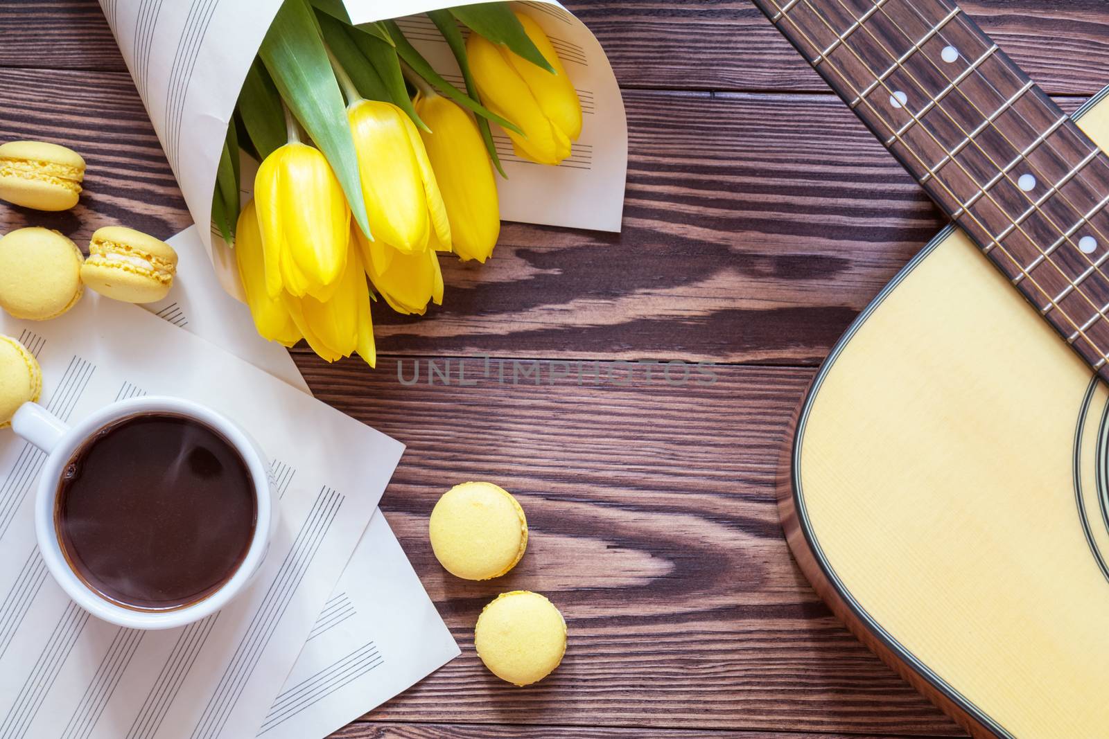 Beautiful spring background music. Guitar, yellow tulips, cup of coffee, musical page on a dark wooden background. Shallow depth of field. Coloring photo with soft focus in instagram style.