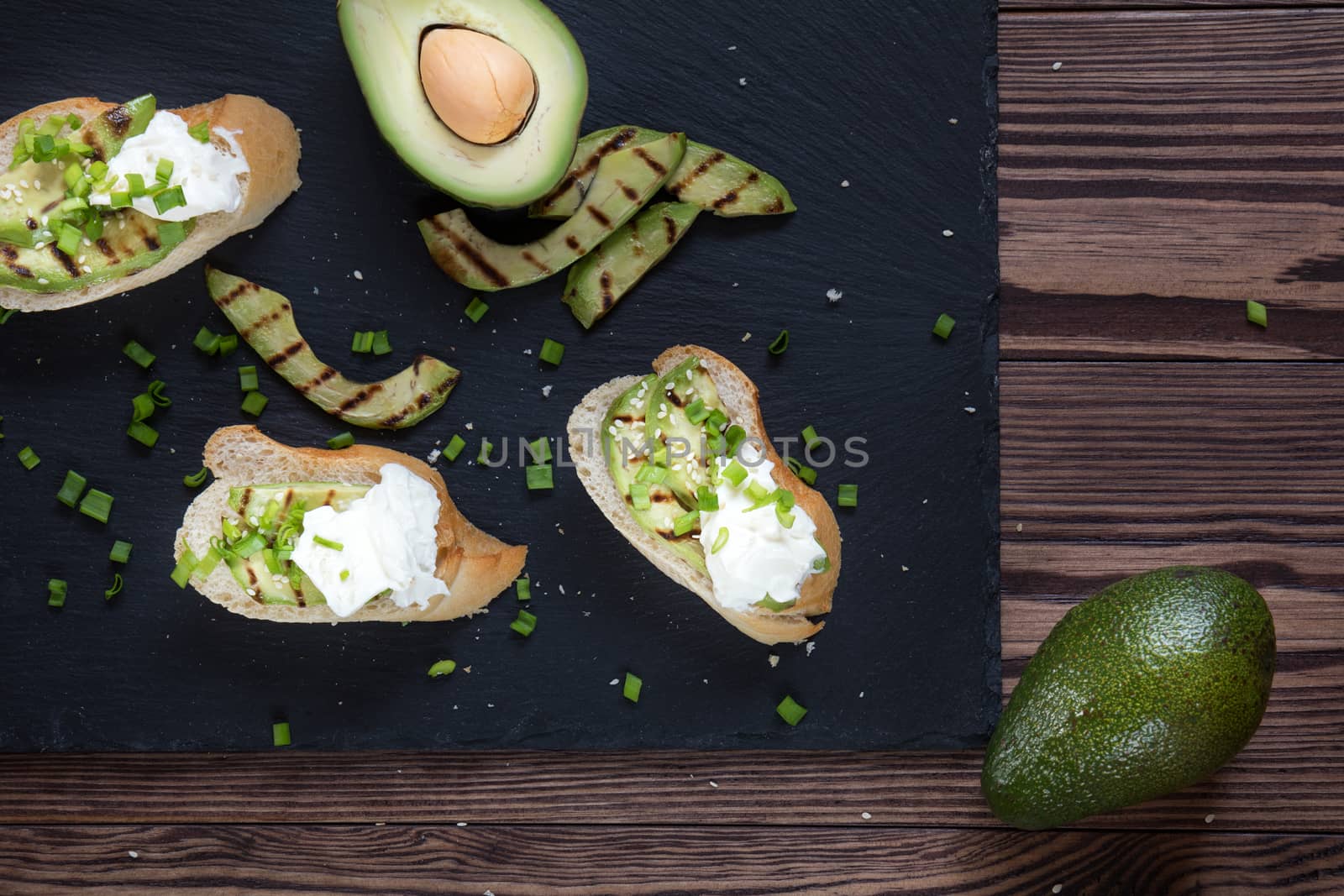 Bread with slices of grilled avocado and cream cheese on a black cutting stone board. Fresh parsley and rosemary. Vegetarian, vegan concept.