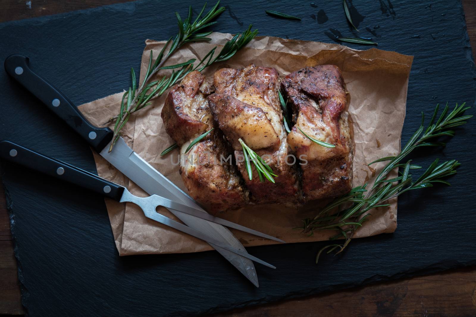 Sliced baked pork with herbs on a stone cutting board on wooden background.Grilled steak on a paper with rosemary  on a dark groundwork.