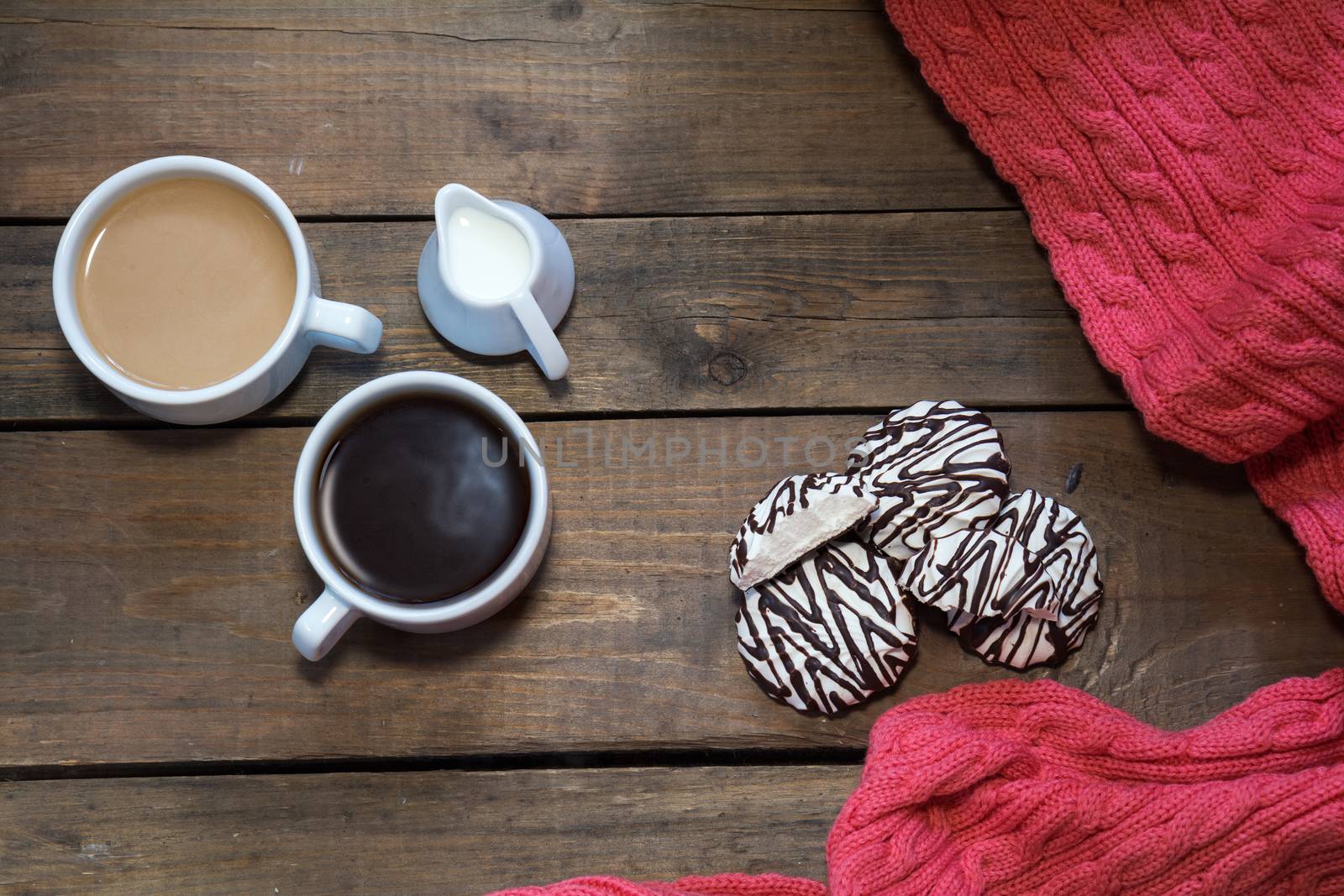 Cup of black coffee, cup of coffee with milk, cream. Pink woven scarf. Marshmallow with chocolate. Dark wooden background. Beautiful vintage coffee groundwork. Coloring and processing photo.