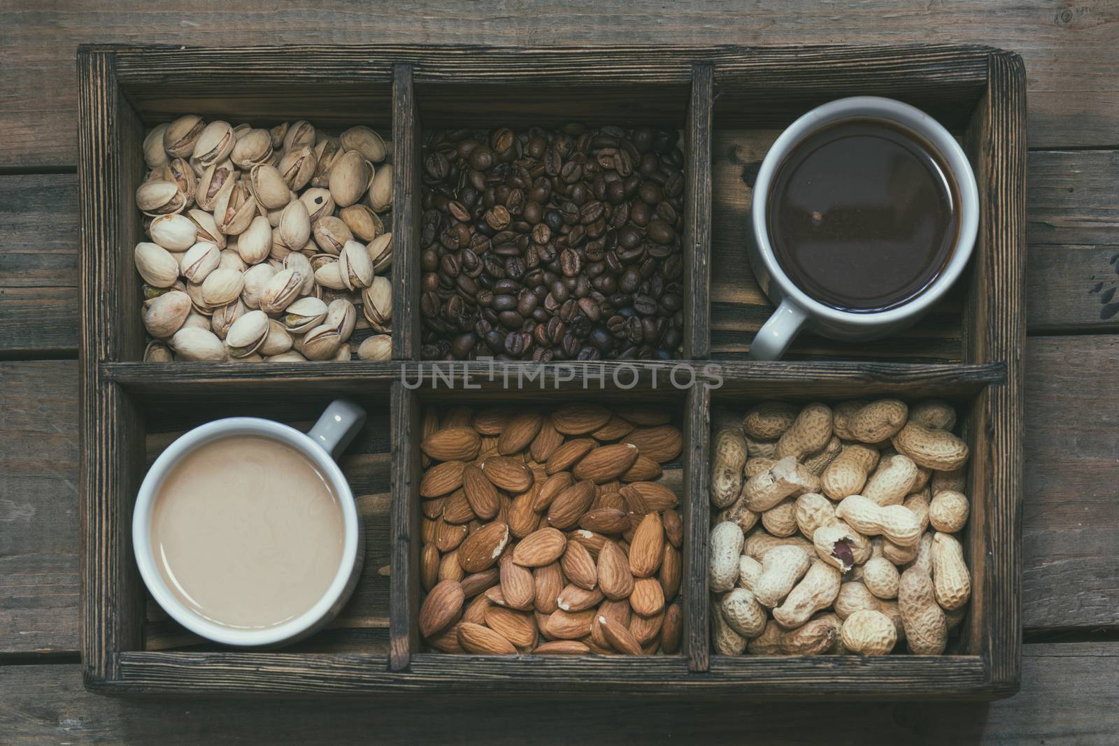 Cup of black coffee, cup of coffee with milk, almond, pistachios, peanut and coffee beans in box. Dark wooden background. Beautiful vintage coffee groundwork. Coloring and processing photo.