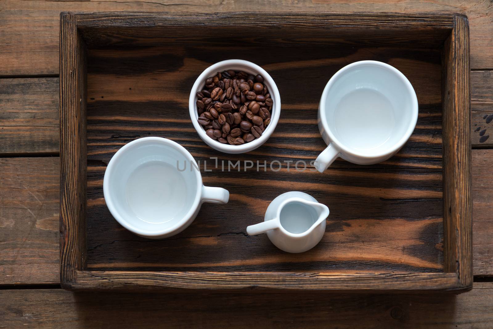 Two white cup, cream and coffee beans in box. Dark wooden background. Beautiful vintage coffee groundwork. Coloring and processing photo.