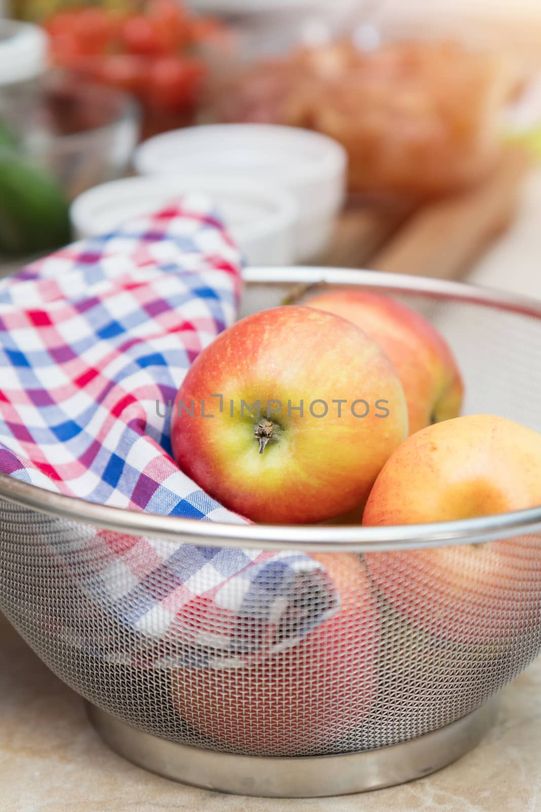 Raw fresh red apple with checkered napkin in sieve in a modern kitchen. Shallow depth of field. Toned.